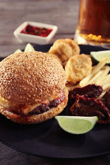 Big tasty hamburger with snacks and glass mug of light beer on wooden table