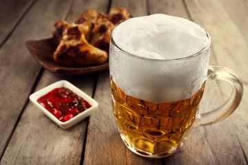 Glass of beer and chicken wings on wooden table, close up