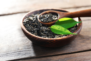 Granulated tea with green leaves in wooden bowl on table closeup