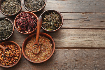 Variety of tea in round bowls with spoon on wooden table, top view