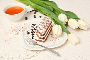 Sweet creamy cake with flowers and present box on wooden table closeup