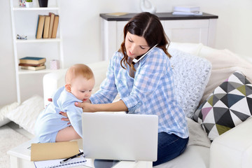 Beautiful woman with baby boy working from home using laptop and mobile phone