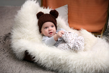 Fototapeta premium Adorable baby in brown knitted hat in luggage bag in the room, close up