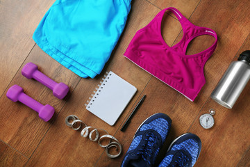 Athlete's set with female clothing, bottle of water, equipment and notebook on wooden background