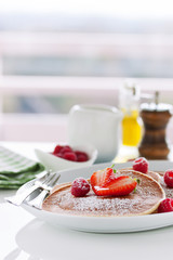Homemade buttermilk american pancakes with fresh strawberry and raspberry on a white plate on a white table for breakfast, closeup, selective focus..