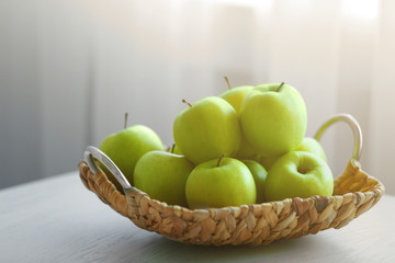 Ripe green apples in a wicker basket on a kitchen table
