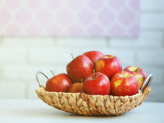 Ripe red apples in wicker basket on a kitchen table