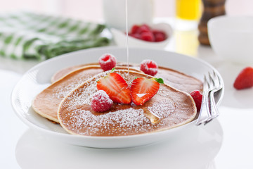 Homemade buttermilk american pancakes with fresh strawberry, raspberry and honey on a white plate on a white table for breakfast, closeup, selective focus..