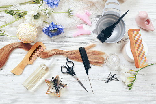 Strand of hair with flowers, barber equipment and tools on light wooden background