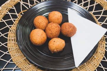 Deep fried balls made from green banana sitting on black plate, traditional latin american food, classy table setting © Fotos 593