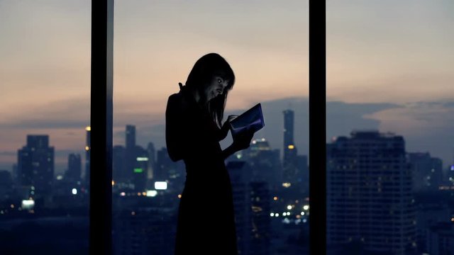 Young woman with tablet computer standing by window at night
