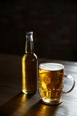Glass mug of light beer with bottle on wooden table