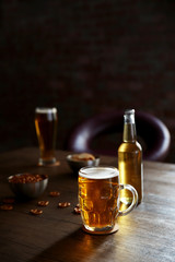Glass mug of light beer with bottle and snacks on wooden table