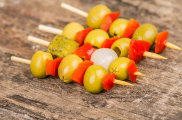 Vegetable skewers of olives, capiscum, pickles and baby onions lying on grey stone surface as seen from above