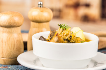 Classy serving of potato soup with meat and vegatables, served in white bowls sitting on table, blue tablecloth, salt pepper shakers, cozy restaurant background