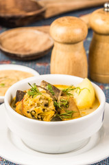 Classy serving of potato soup with meat and vegatables, served in white bowls sitting on table, blue tablecloth, salt pepper shakers, cozy restaurant background
