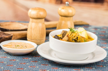 Classy serving of potato soup with meat and vegatables, served in white bowls sitting on table, blue tablecloth, salt pepper shakers, cozy restaurant background