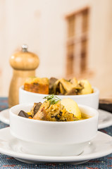 Classy serving of potato soup with meat and vegatables, served in white bowls sitting on table, blue tablecloth, salt pepper shakers, cozy restaurant background