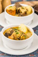Classy serving of potato soup with meat and vegatables, served in white bowls sitting on table, blue tablecloth, cozy restaurant background