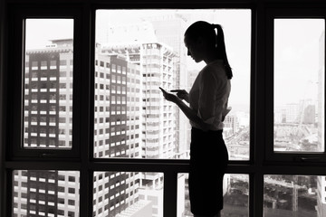 Business woman on her smartphone standing next to office window. 