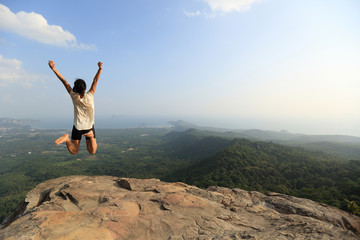  cheering young asian woman jumping on mountain peak rock