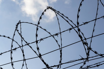 Prison wall barbed wire fence detail with blue sky in background