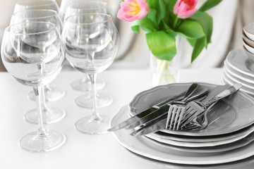 Stack of plates, cutlery with bouquet of tulips on a table.