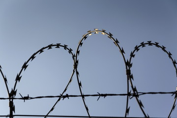 Prison wall barbed wire fence detail with blue sky in background