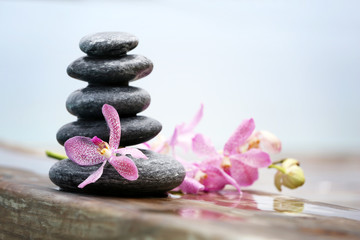 Fototapeta na wymiar Stack of spa stones with pink orchids on wooden wet bridge