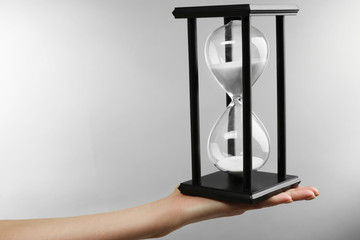 Hourglass in female hand on grey background