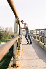 Runner man doing stretching leaning against the railing of a bri