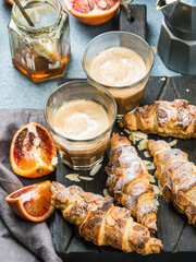 Traditional Italian style home breakfast. Latte in glasses, almond croissants and red bloody Sicilian oranges over concrete textured table