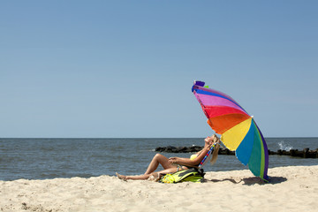 Woman enjoying a day at the beach with snorkeling gear,sitting a a lounge chair under a colorful rainbow striped umbrella