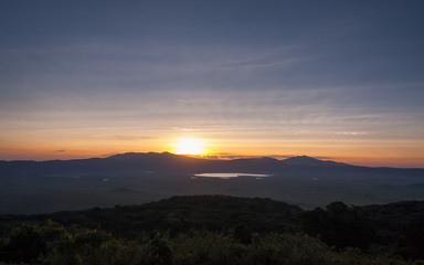 Panoramic view of huge Ngorongoro caldera (extinct volcano crater) with setting Sun against evening glow background at dusk. Great Rift Valley, Tanzania, East Africa.
