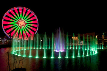 Ferris Wheel during the Christmas Holidays taken at night with long exposure with colorful water fountain in foreground taken at night with long exposure.
