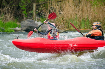 Two kayakers paddling hard the kayak with lots of splashes.  active kayakers on the rough water. alloy high speed, motion blur, active family rest in the spring
