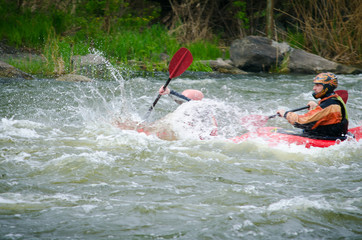 Two kayakers paddling hard the kayak with lots of splashes.  active kayakers on the rough water. alloy high speed, motion blur, active family rest in the spring
