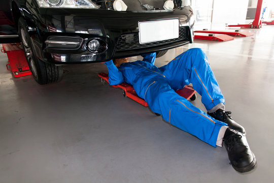 Mechanic in blue uniform lying down and working under car at the