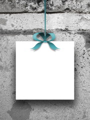 Close-up of one square blank frame hanged by aqua ribbon against old stone wall background