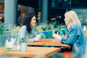 Two friends talking and drinking coffee, sitting in a cafe outdo
