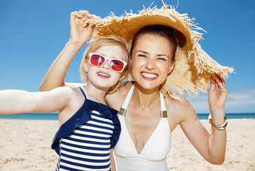 Happy mother and daughter under big straw hat taking selfie