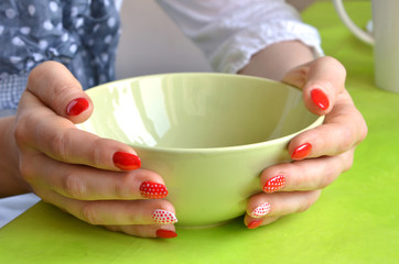 Girl with red nails with dots on her fingers hold green bowl, closeup