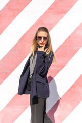 Fashion  girl posing over Red white striped wall background. Beauty woman with pink lips make-up posing on the street.