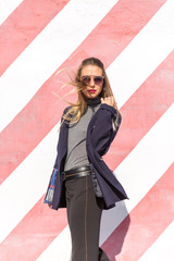 Fashion  girl posing over Red white striped wall background. Beauty woman with pink lips make-up posing on the street.