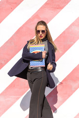 Fashion  girl posing over Red white striped wall background. Beauty woman with pink lips make-up posing on the street.