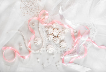French meringue cookies for wedding background with pearls, pink and white satin ribbons and lace, flat lay, top view