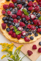 Fresh berries on the tart cake from above. Delicious homemade pie with organic raspberries and blueberries and summer flowers on wooden board. Summer dessert and snack.