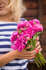 Fototapeta na wymiar Beautiful bouquet of dark pink peonies in woman hands on a wooden background. Bunch of flowers in hands. Stripes. Summer time.