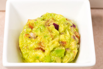 Delicious guacamole dip in white bowl.