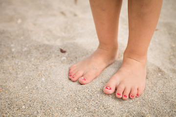 Obraz na płótnie Canvas Closeup of a little girl's legs and feet walking on the sand of the beach with the sea water in the background summer